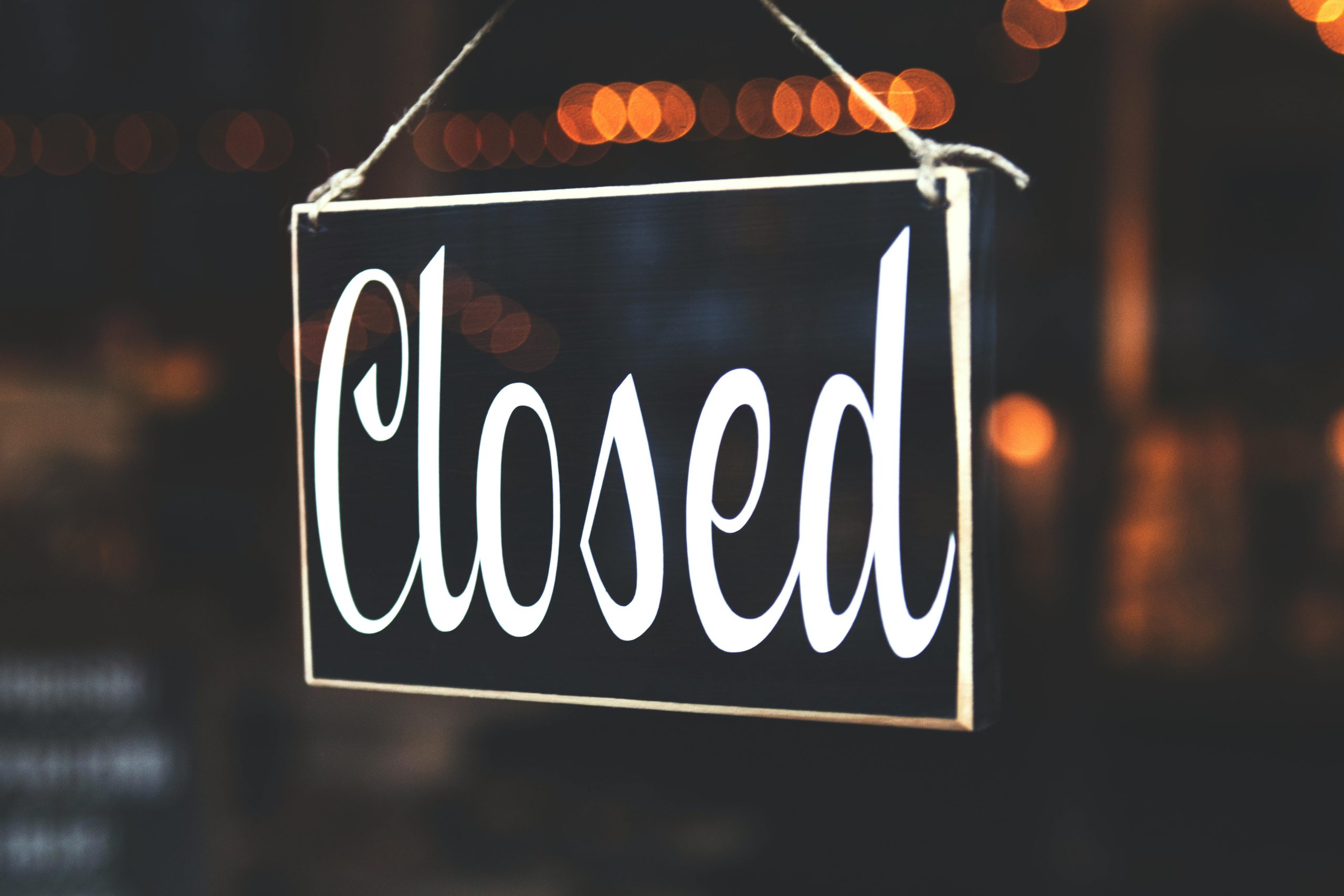 A close-up of a 'Closed' sign hanging against a blurred, bokeh background, creating a warm, inviting atmosphere.