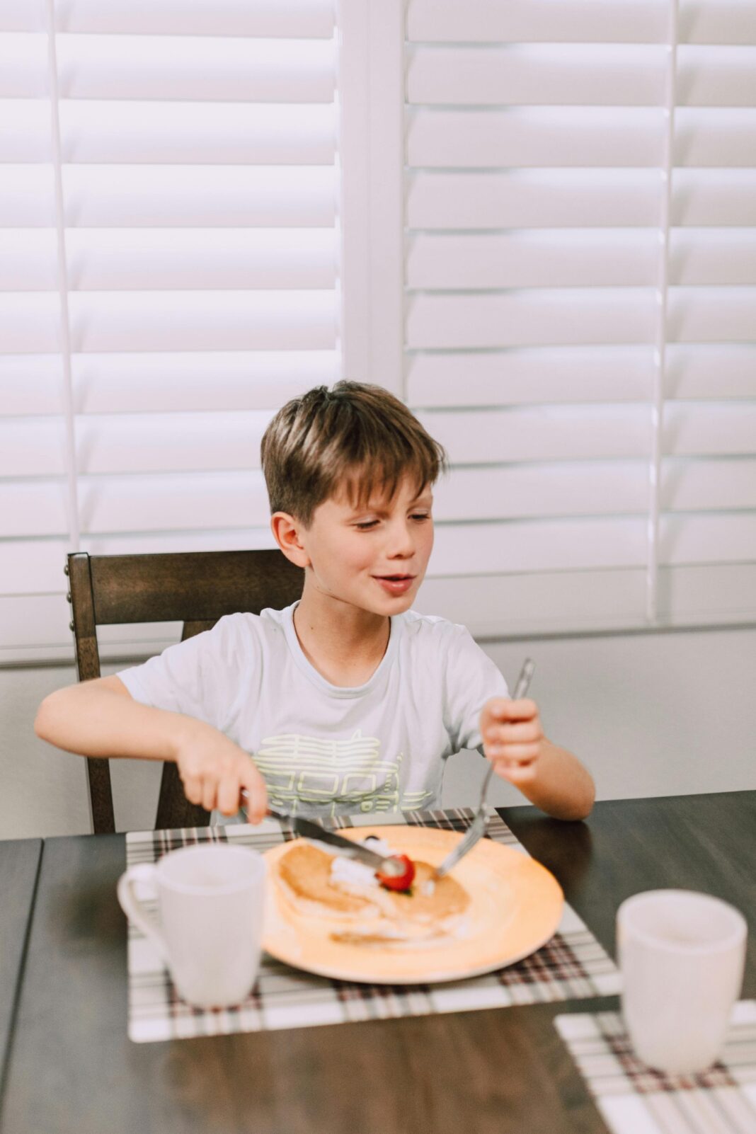 A child enjoying a breakfast meal at a dining table using utensils.