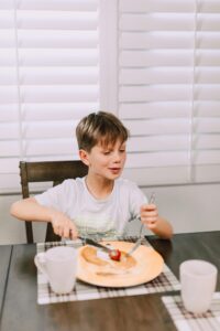 A child enjoying a breakfast meal at a dining table using utensils.